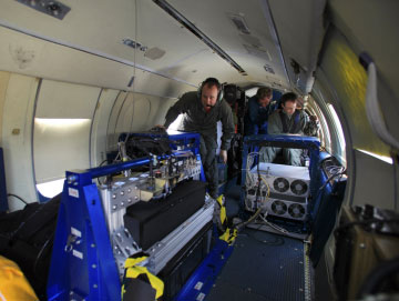 image shows the interior of the falcon aircraft and a large instrument being installed by personnel