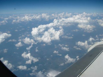 image shows a view out the window of the falcon aircraft over Texas. many small clouds are visible in the sky below the aircraft.